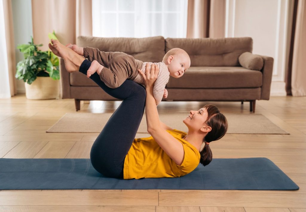 Mother performing gentle postpartum exercise while holding her baby, illustrating chiropractic-supported recovery in Sydney.