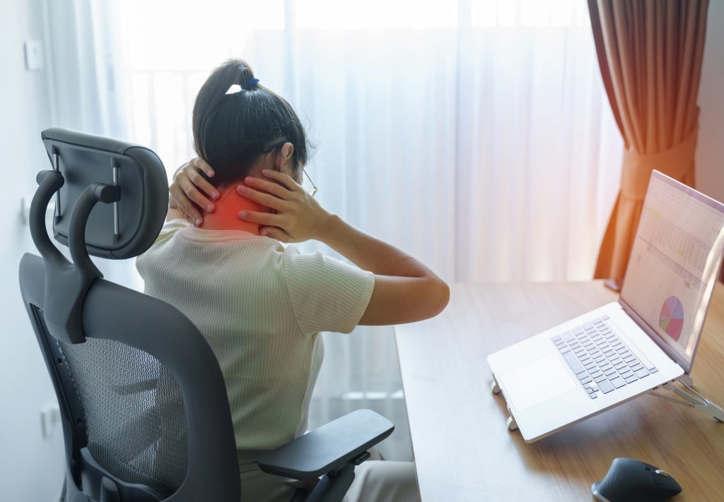 Woman experiencing neck pain at an office desk, emphasizing the importance of workplace ergonomics and chiropractic solutions in Sydney.