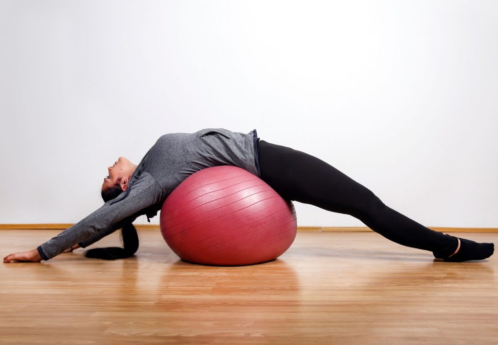 Woman stretching her back over a stability ball for spinal flexibility, posture correction, and chiropractic support in Sydney.